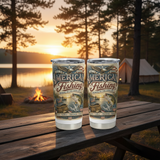 Two American Fishing-themed tumblers with an eagle and bass design on a picnic table at a lakeside campground